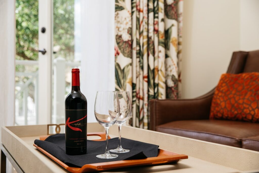 wine bottle and two wine glasses on tray next to brown leather couch